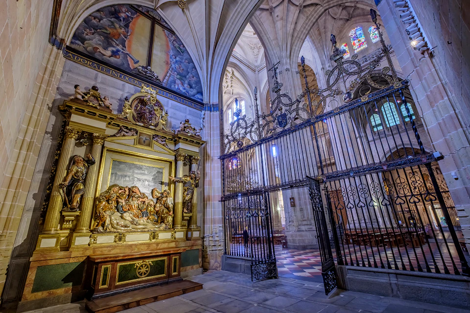 Intricately detailed cathedral interior with ornate iron gates, stained glass windows, and a golden religious altar adorned with sculptures.