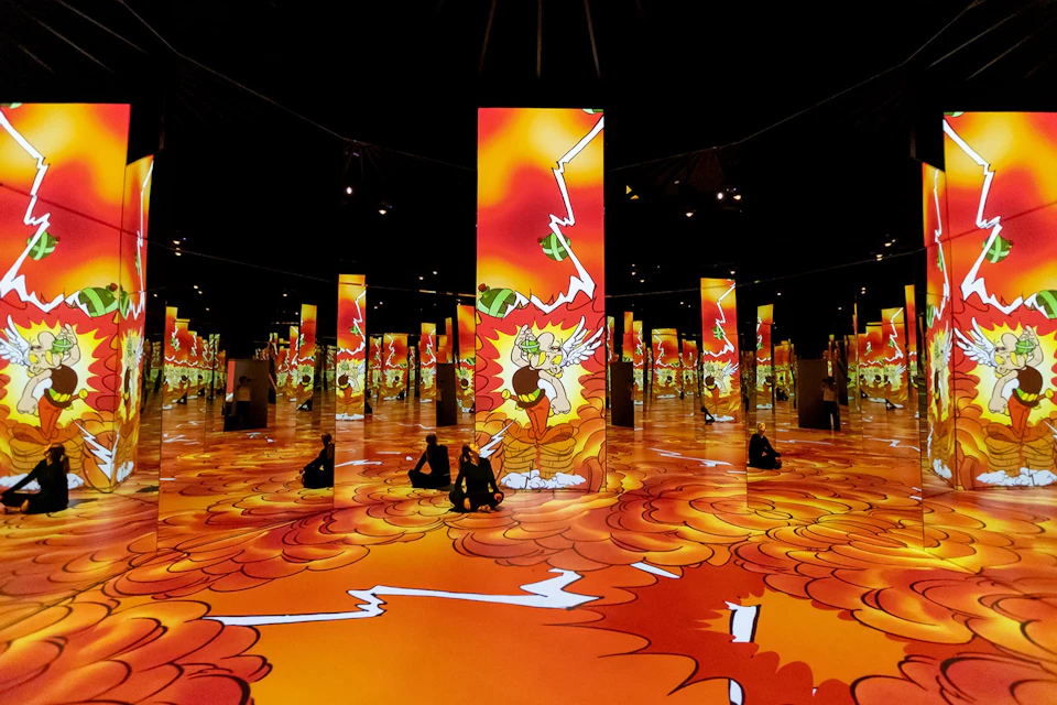A room with bright animated projections of a cartoon character and orange clouds on the walls, floor, and vertical columns.