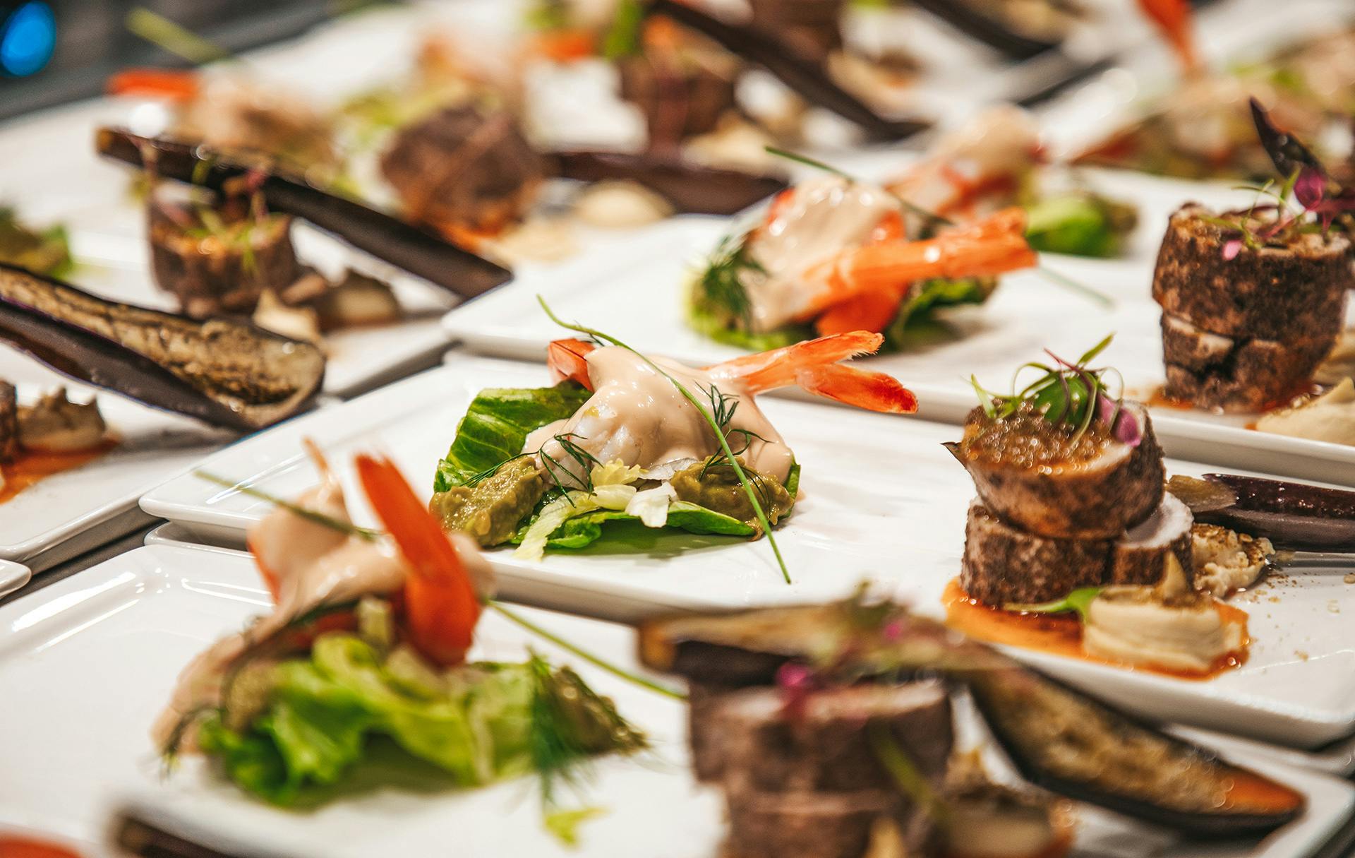 양상추에 새우를 올리고 고기에 물린 고기를 포함한 다양한 고급 애피타이저가 흰색 접시에 배열되어 있습니다.