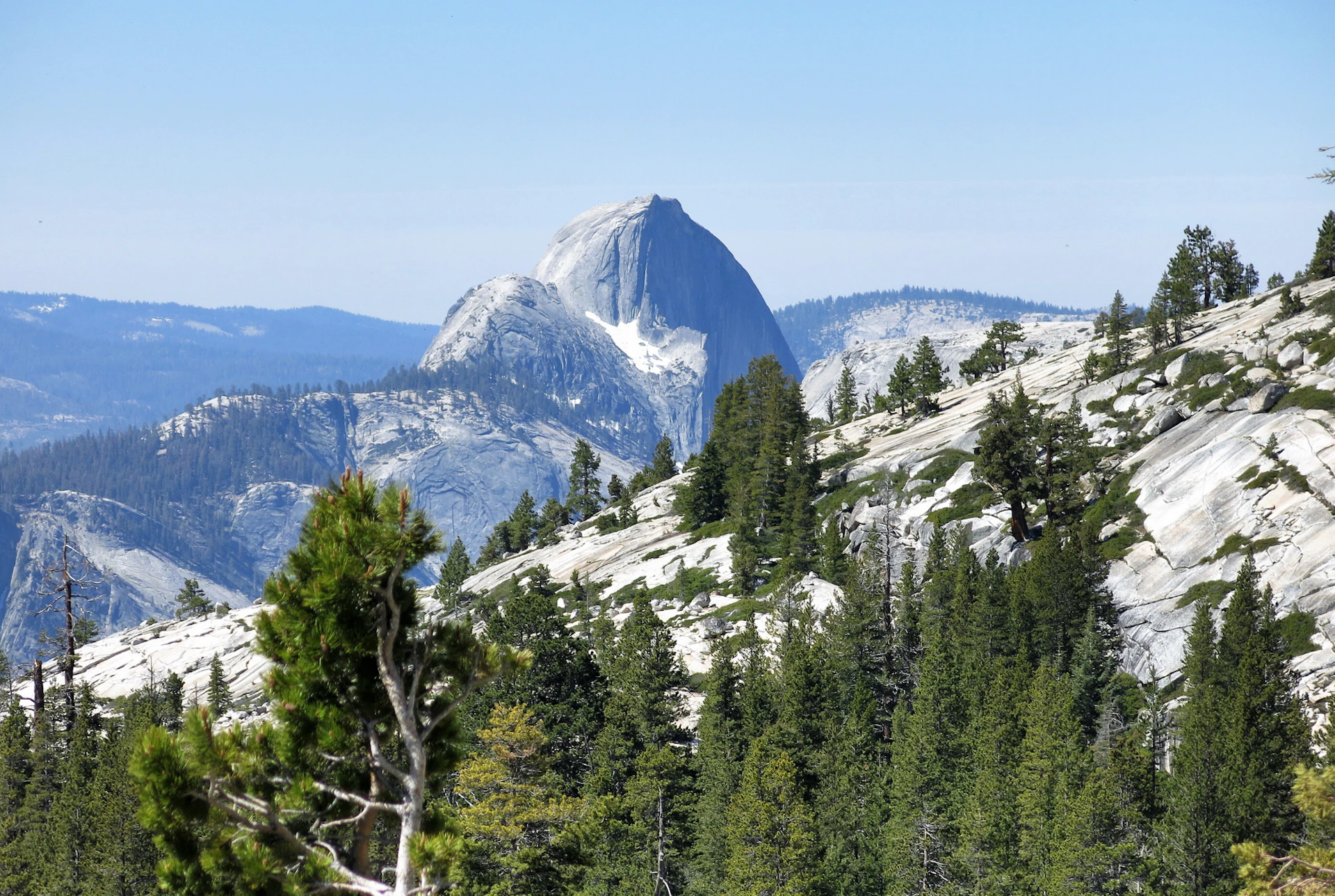 Granite dome rises above forested slopes under a clear blue sky.