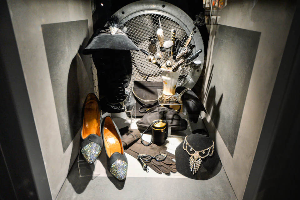 A display case with black fashion accessories including shoes, a hat, gloves, a necklace, and a jewelry holder shaped like a hand.