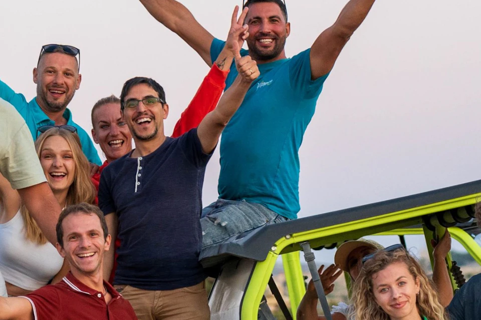 A group of people posing energetically around an off-road vehicle in an outdoor setting during sunset.