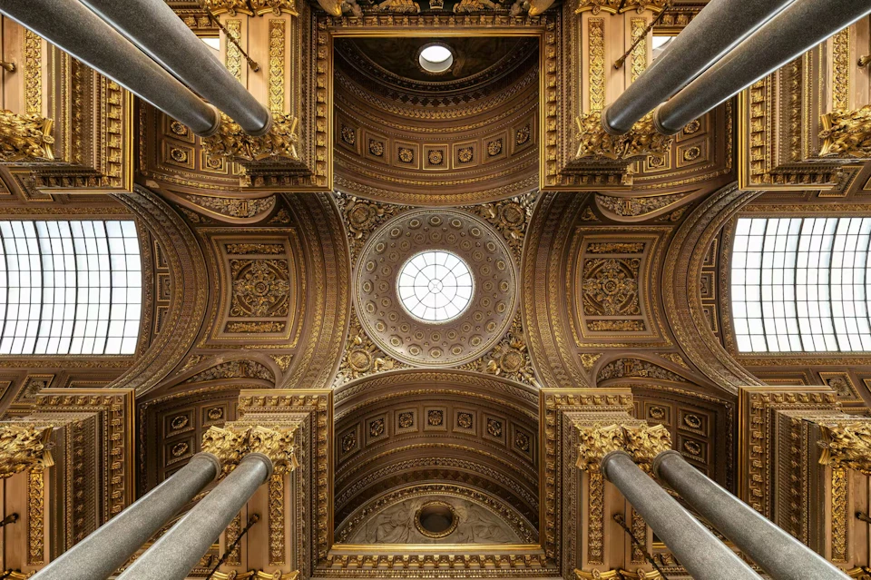 Ornate ceiling with a central circular skylight, surrounded by decorative arches and columns with gold accents.