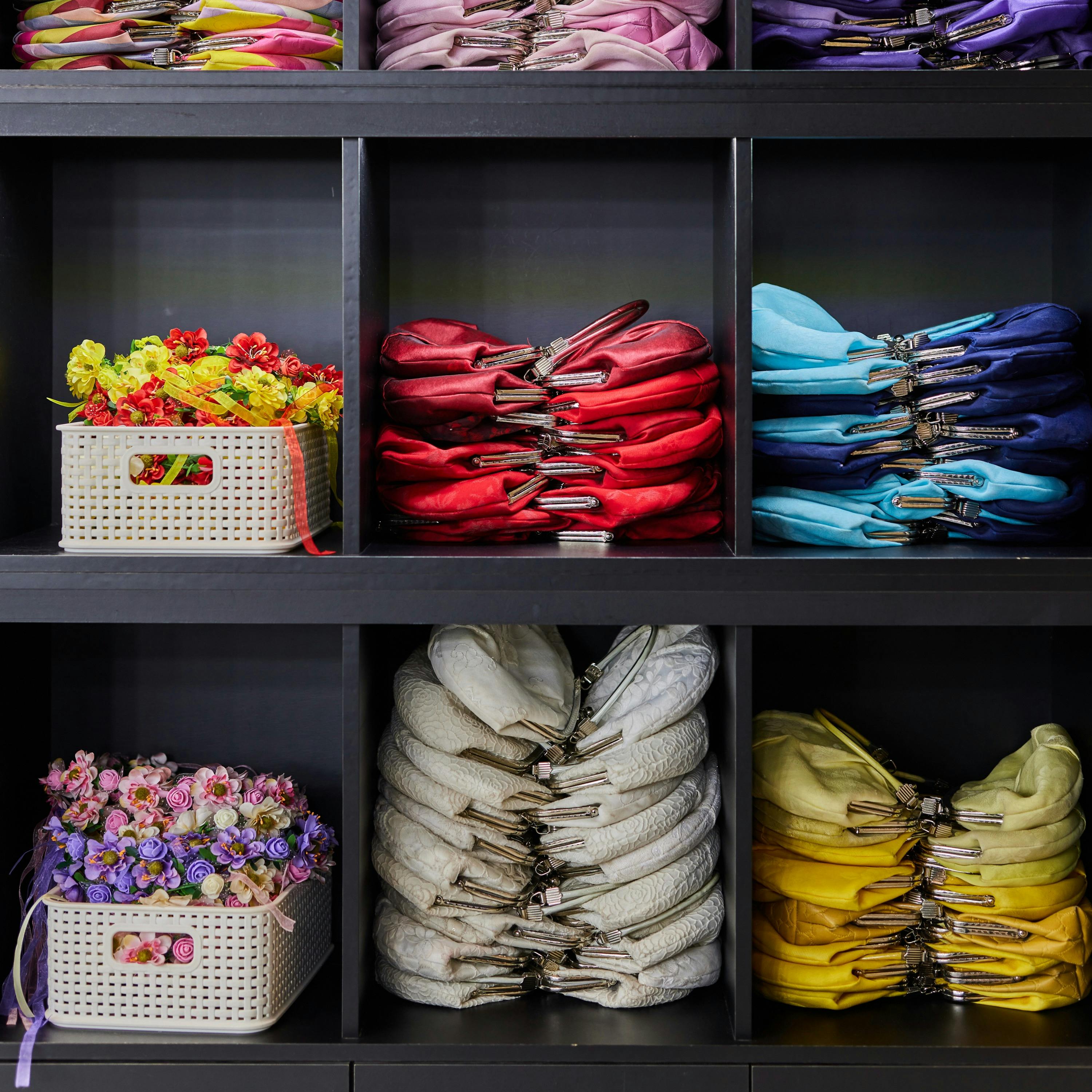 A neatly organized shelf displaying colorful folded fabric and baskets of artificial flowers.