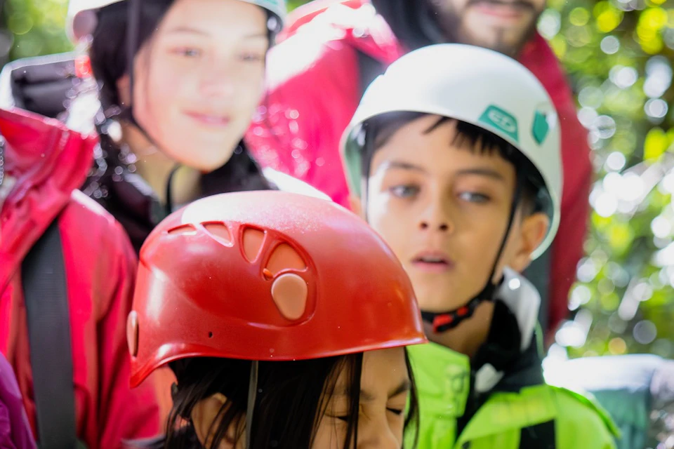 A group of people wearing safety gear observe a bird perched on a child's hand in an outdoor setting.