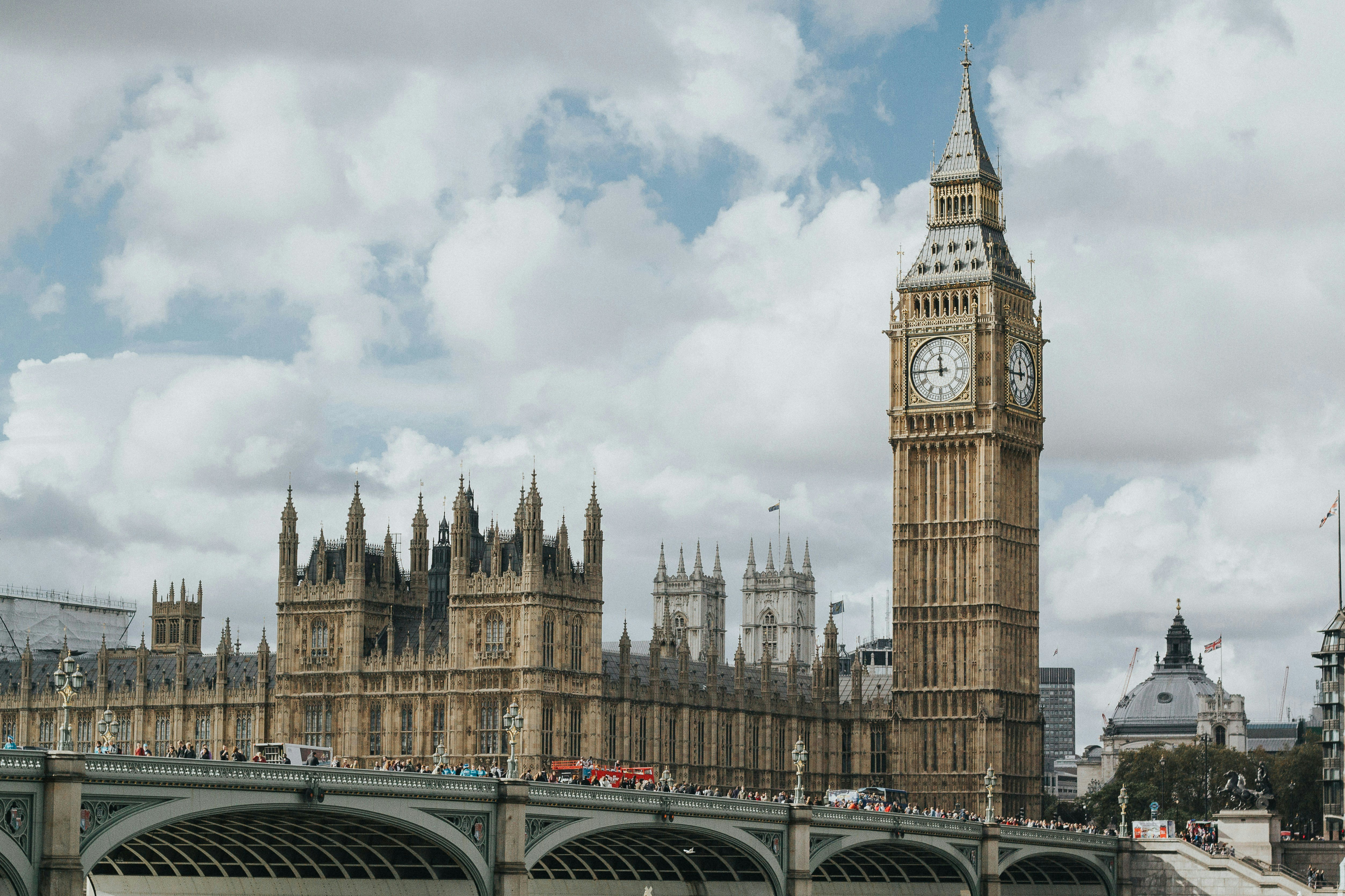 Big Ben a budovy parlamentu s výhledem přes Westminsterský most a zamračenou oblohou v pozadí.