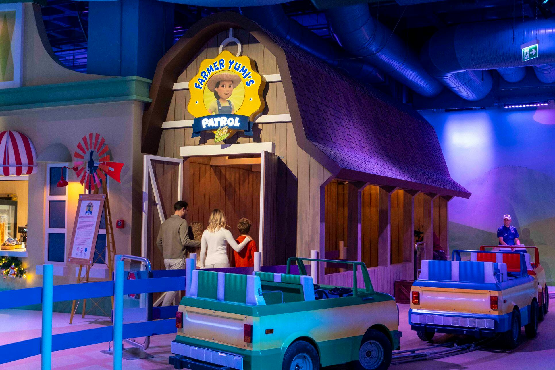 Een familie die een attractie met schuurthema 'Farmer Yumi's Patrol' binnengaat met een kleine auto op de voorgrond.