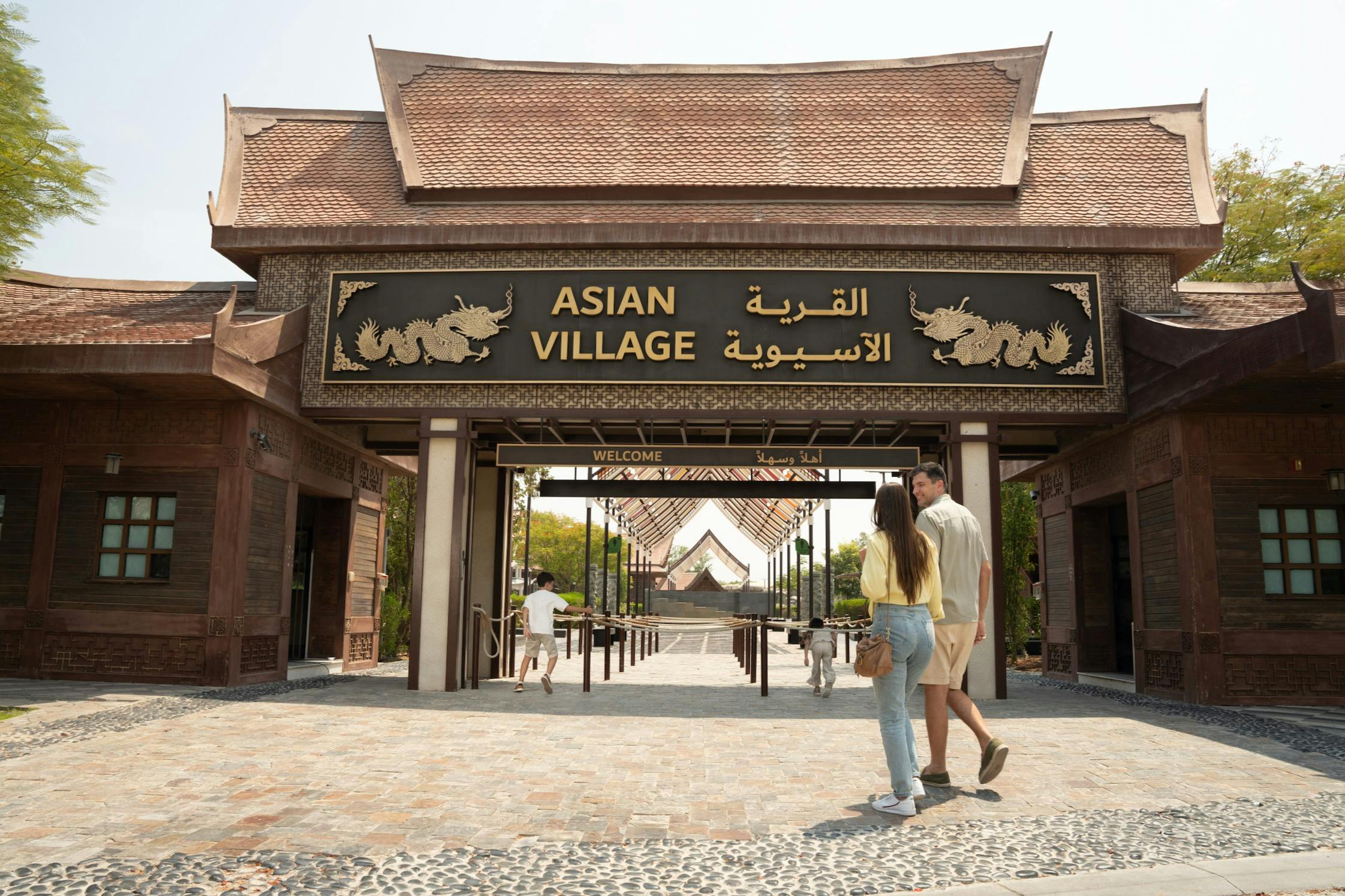 Ένα ζευγάρι περπατά προς την είσοδο του "Ασιατικού Χωριού", που διαθέτει μια μεγάλη παραδοσιακή πύλη με σήμανση στα αγγλικά και τα αραβικά.