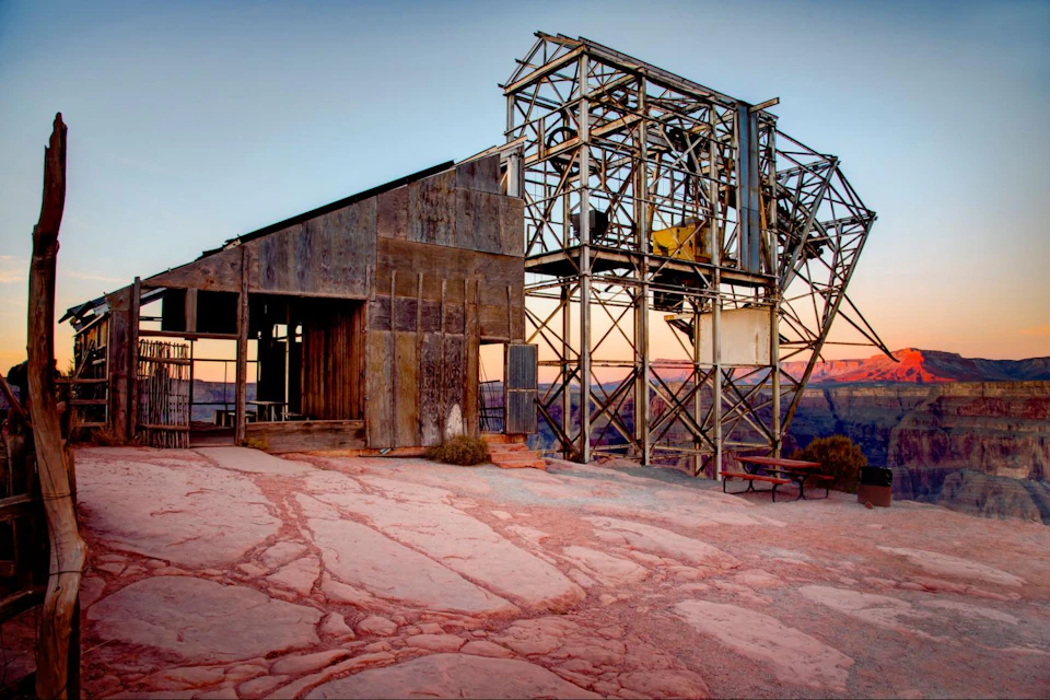 Rustic wooden and metal structure with a steel framework set against a scenic canyon backdrop at dusk.