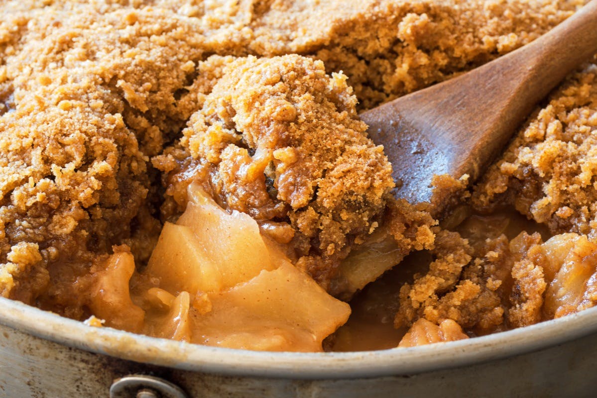 Κοντινό πλάνο από ένα χρυσό-καφέ τραγανό μήλο με μια ξύλινη κουτάλα που κουβαλάει μια μερίδα, δείχνοντας τρυφερά μήλα και εύθρυπτη επικάλυψη.