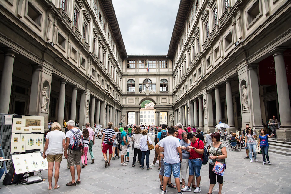 People walking and socializing in a courtyard between two large, symmetrical buildings with columns and arches.