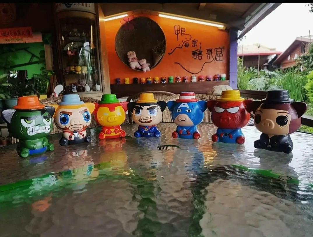 A row of colorful cartoon character figurines wearing hats placed on a glass table, with a decorated background.