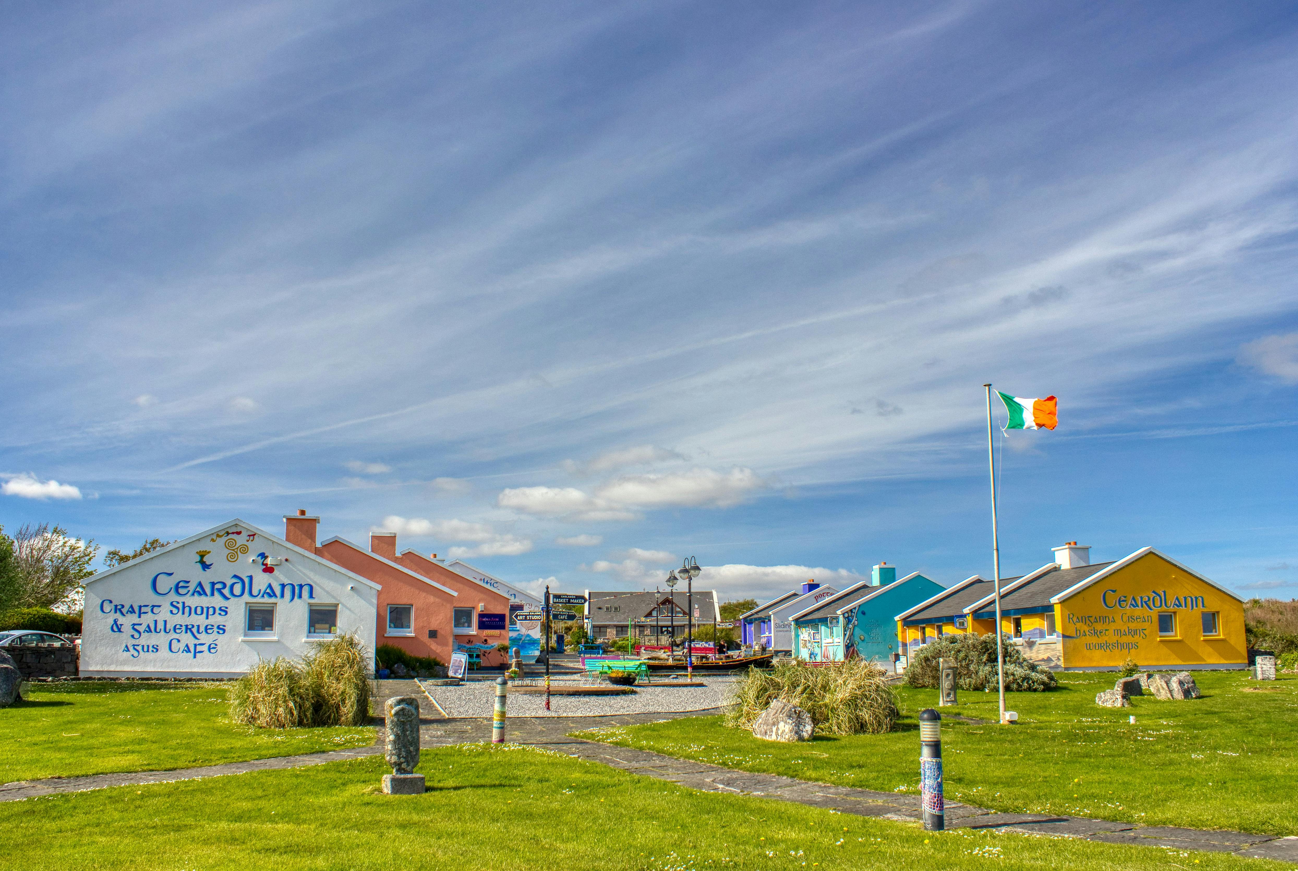 벽화와 아일랜드 국기가 그려진 깃대, 부분적으로 흐린 하늘 아래 푸른 잔디밭이 있는 다채로운 주택이 줄지어 있습니다.