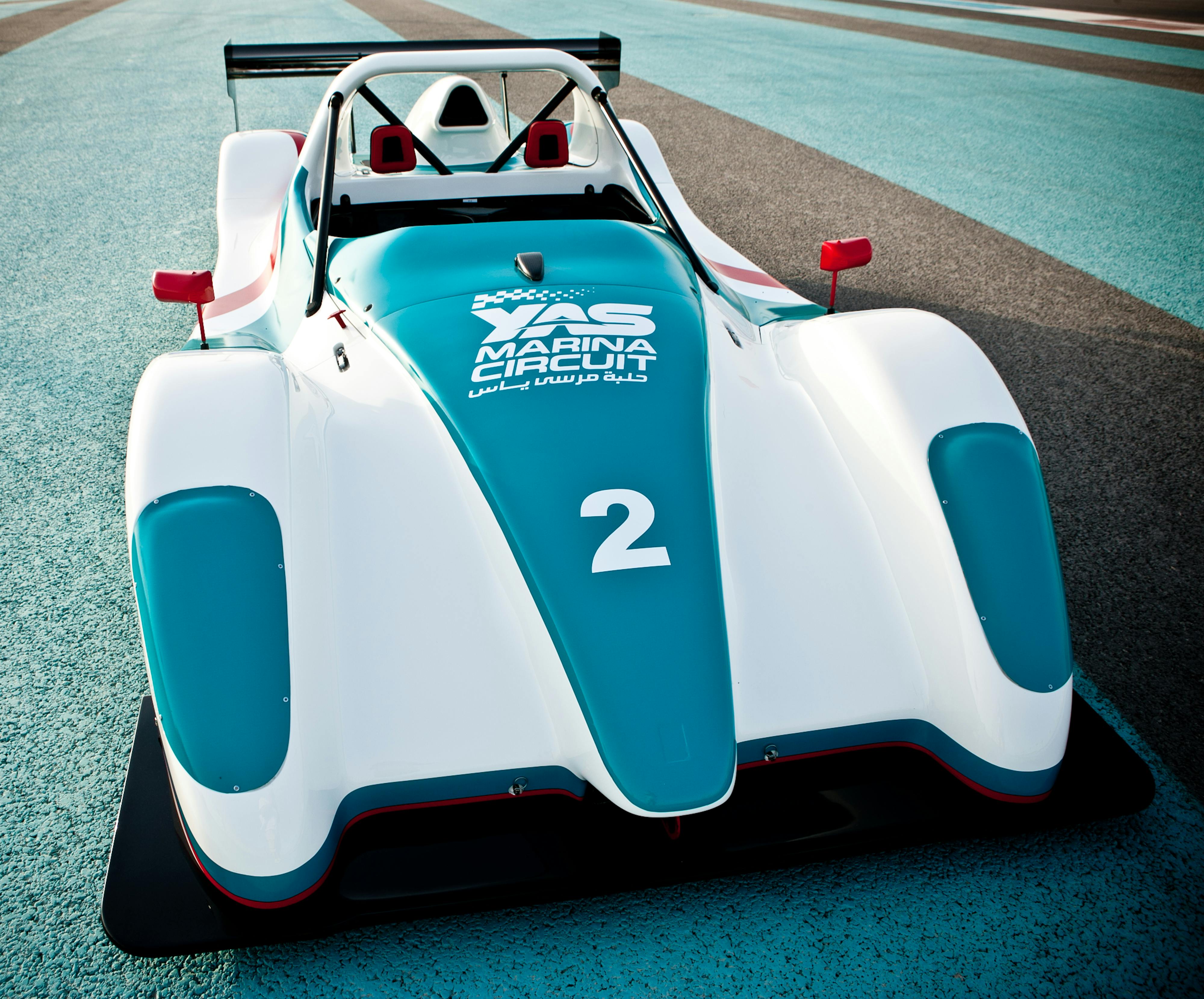 White and turquoise race car with number 2 and "YAS Marina Circuit" printed on the hood, parked on a track.