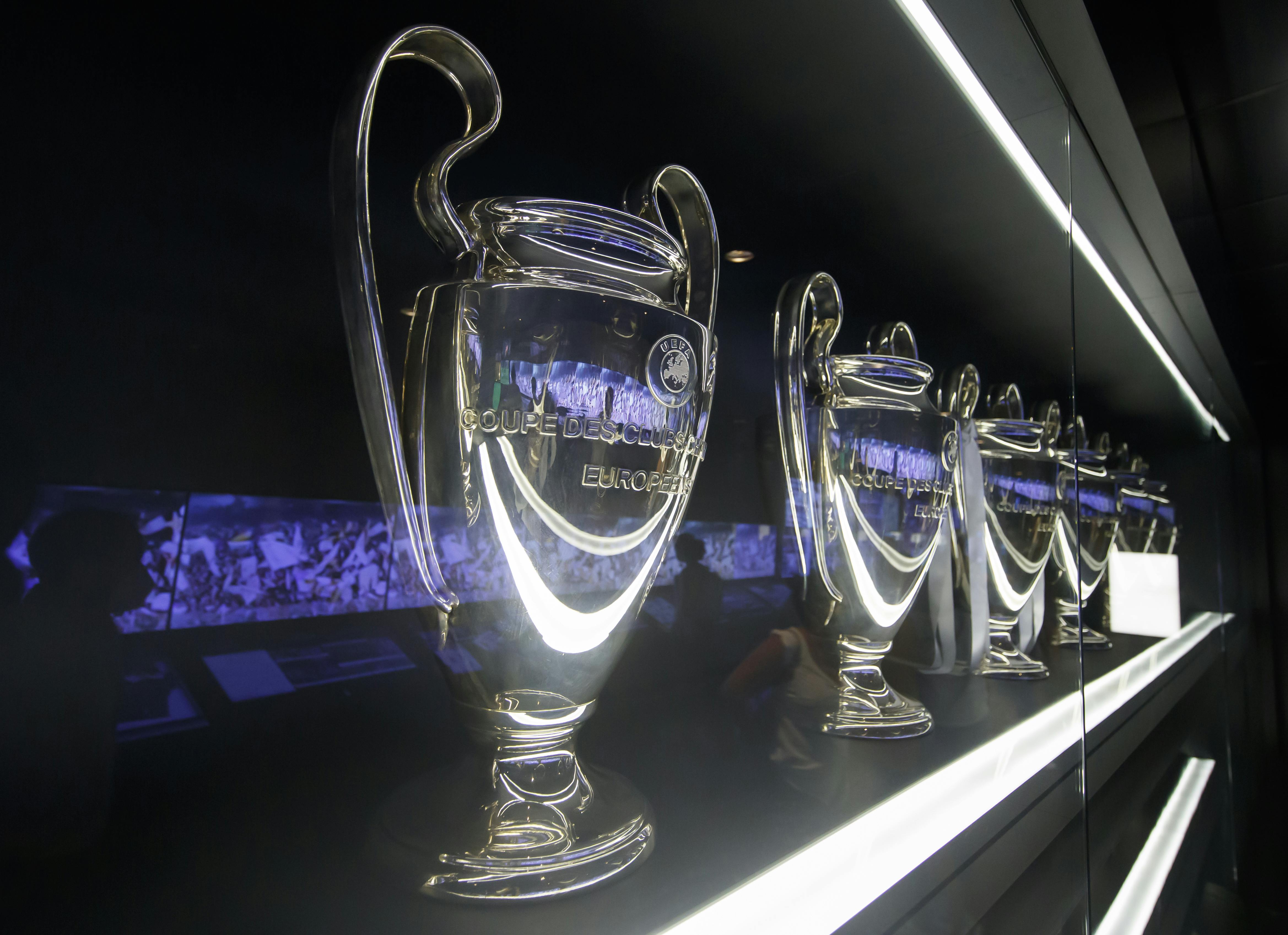 Multiple silver trophies with large handles are displayed in a glass case. The text "Coupe Des Clubs Champions Européens" is visible.