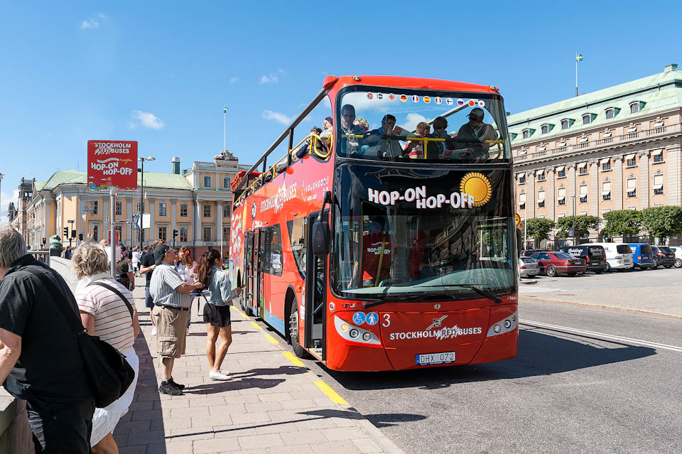 A red double-decker tour bus with "Hop-On Hop-Off" on the front, parked at a curb with people boarding.