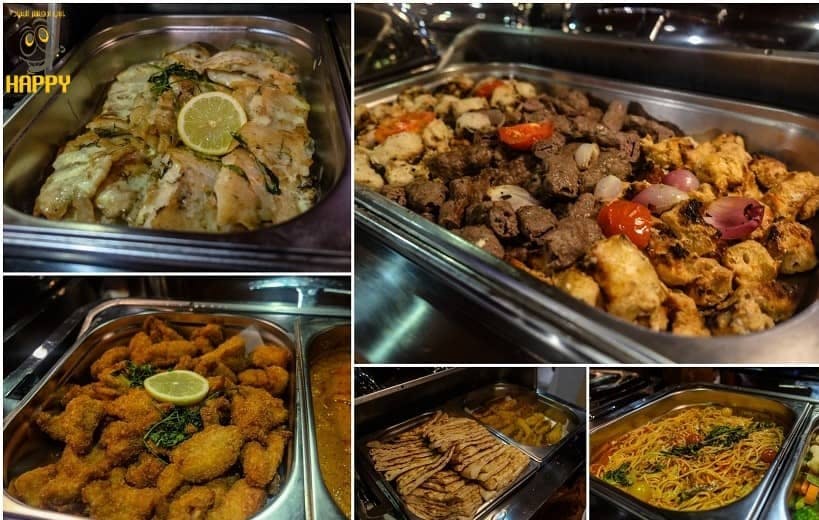 Grande plano de vários tabuleiros de bufete com legumes assados, peixe frito com limão, carne grelhada, pães achatados e massas.