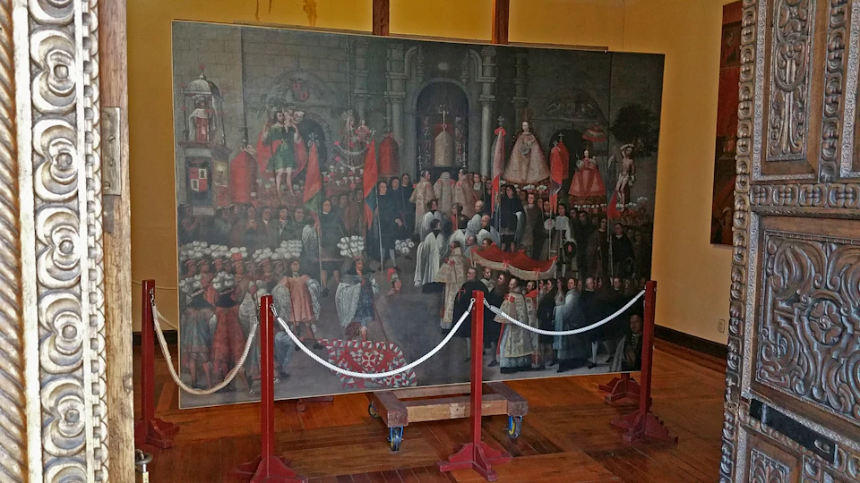 A large historic painting depicting a ceremonial scene with numerous figures, many in elaborate attire, behind a roped-off area.