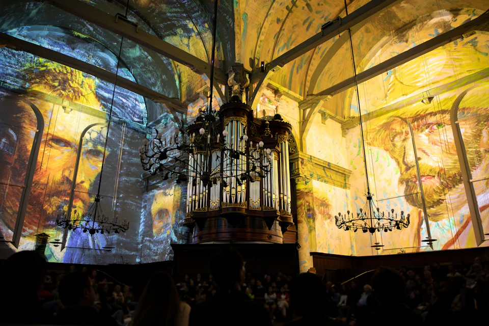 Ornate church interior with stained glass windows, chandeliers, and a large pipe organ. Projection of colourful artwork on walls.