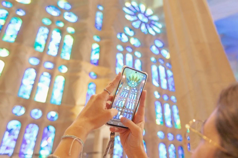 Hands holding a smartphone, capturing a photo of colorful stained glass windows in a cathedral.