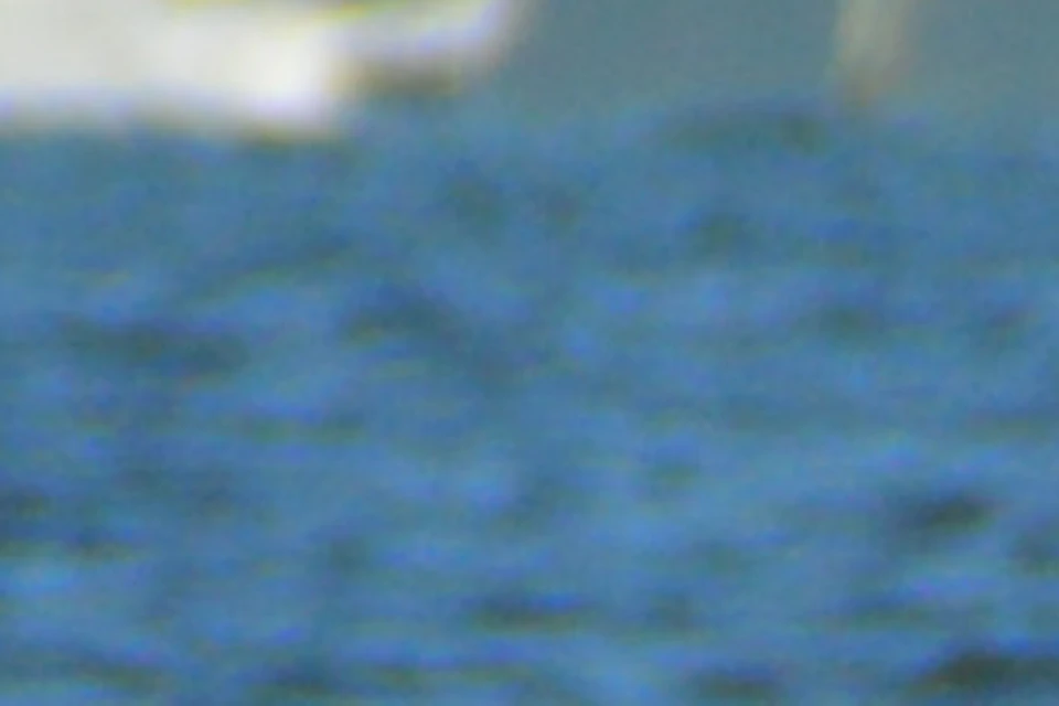 Two people parasailing over water, wearing yellow life vests, with their feet touching the water's surface.