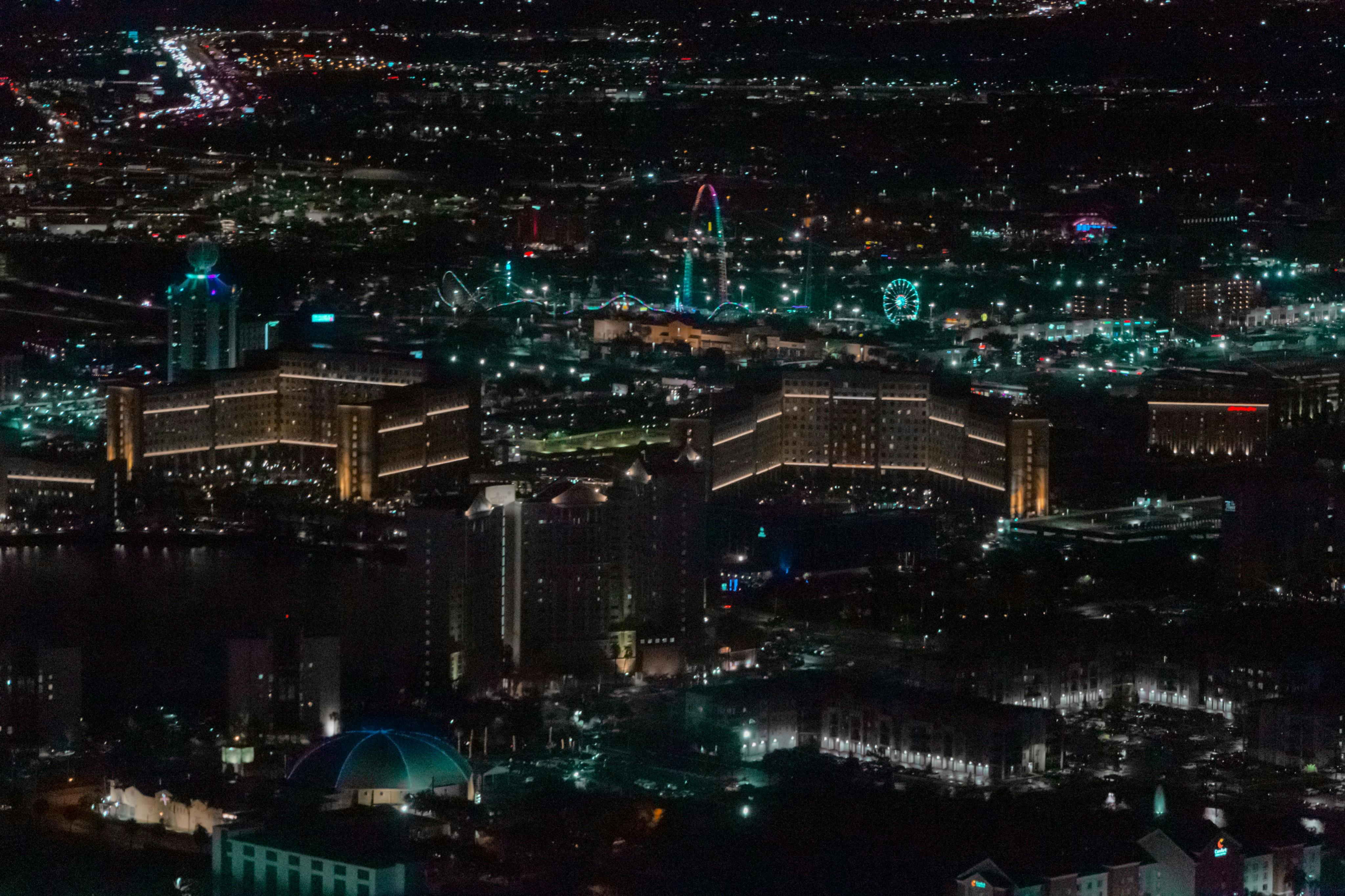 A cityscape at night with illuminated buildings, a brightly lit Ferris wheel, and colorful lights scattered throughout the scene.