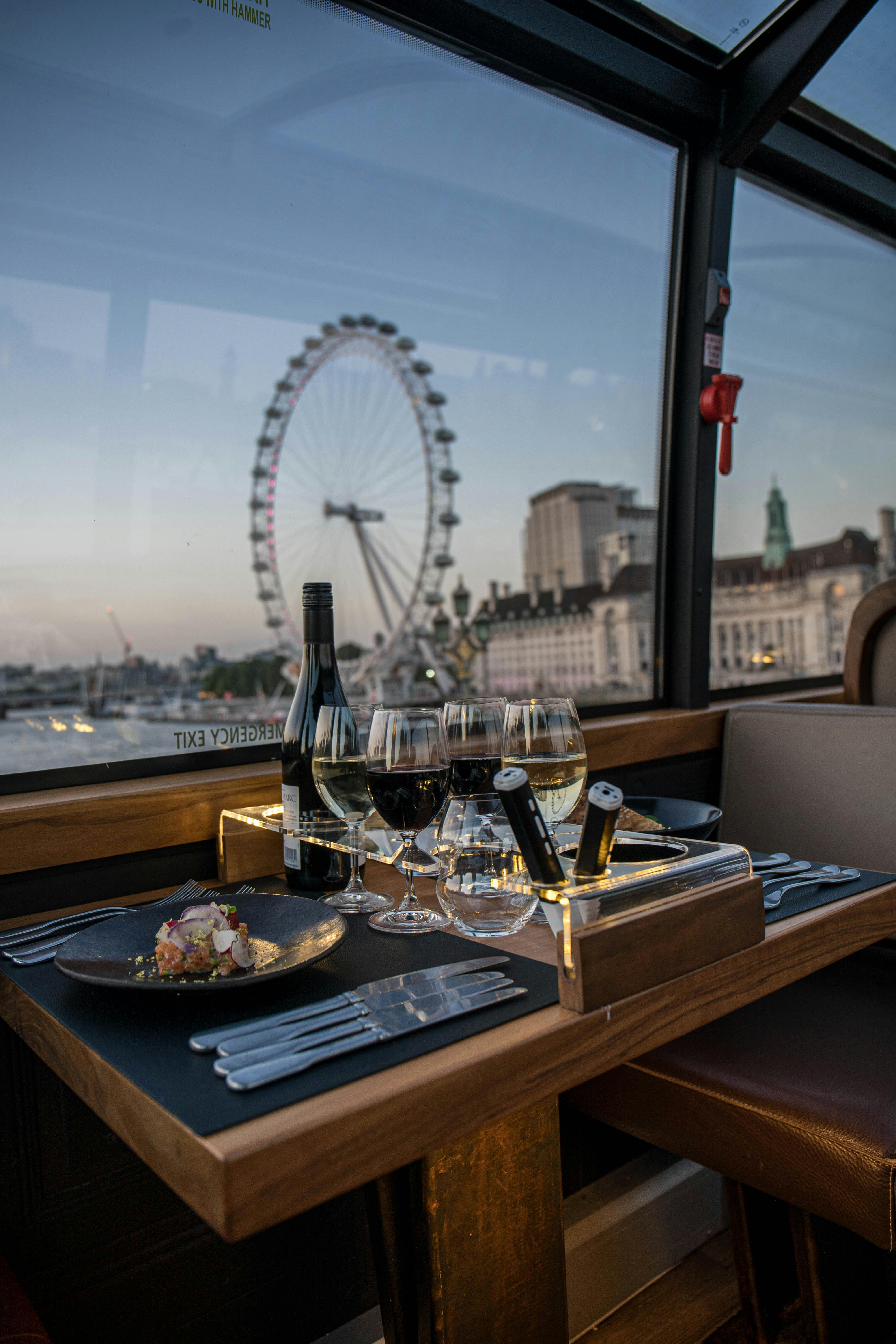 Elegant dining setup on a train with a view of the London Eye and cityscape at dusk.