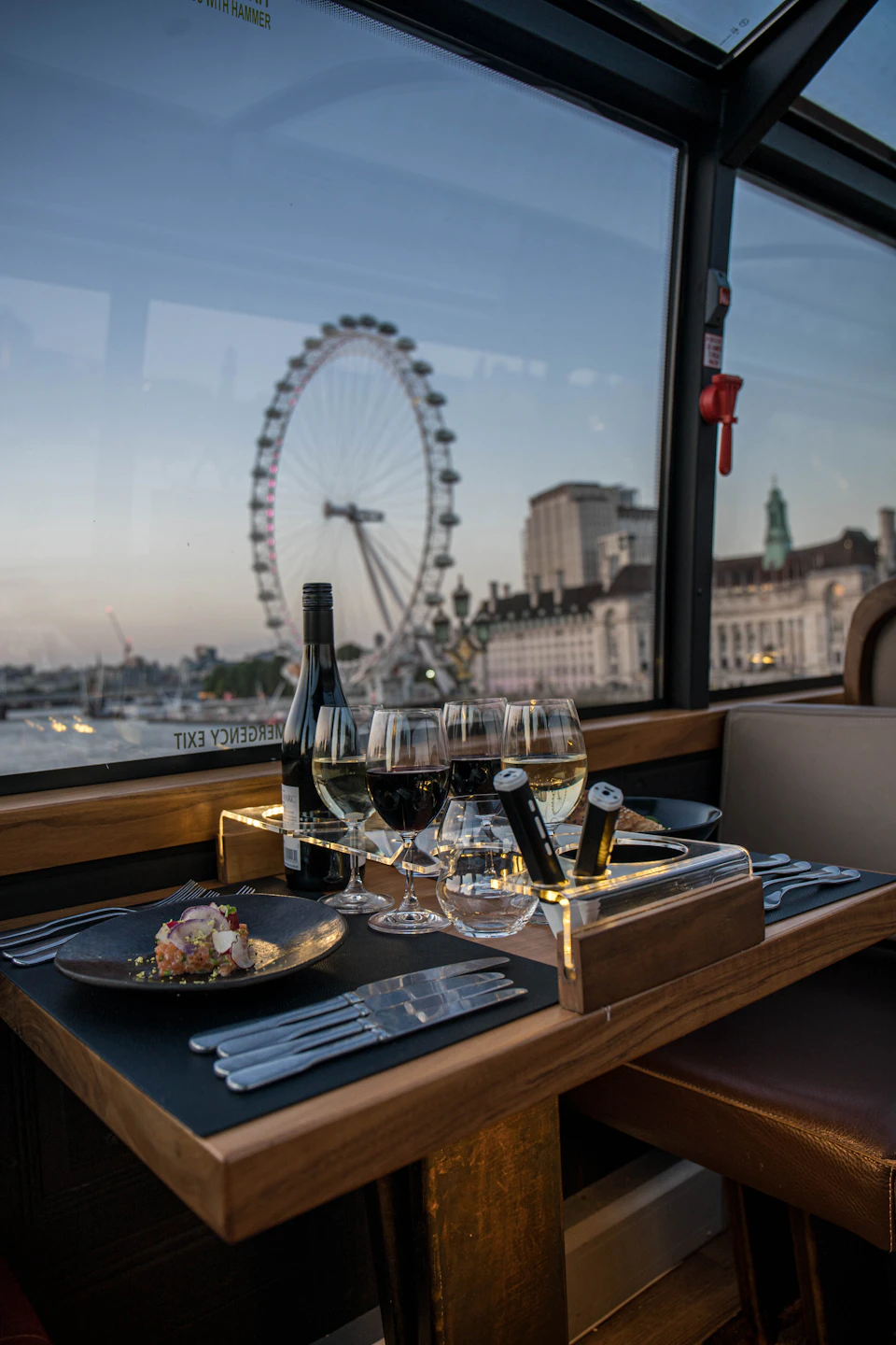 Elegant dining setup on a train with a view of the London Eye and cityscape at dusk.