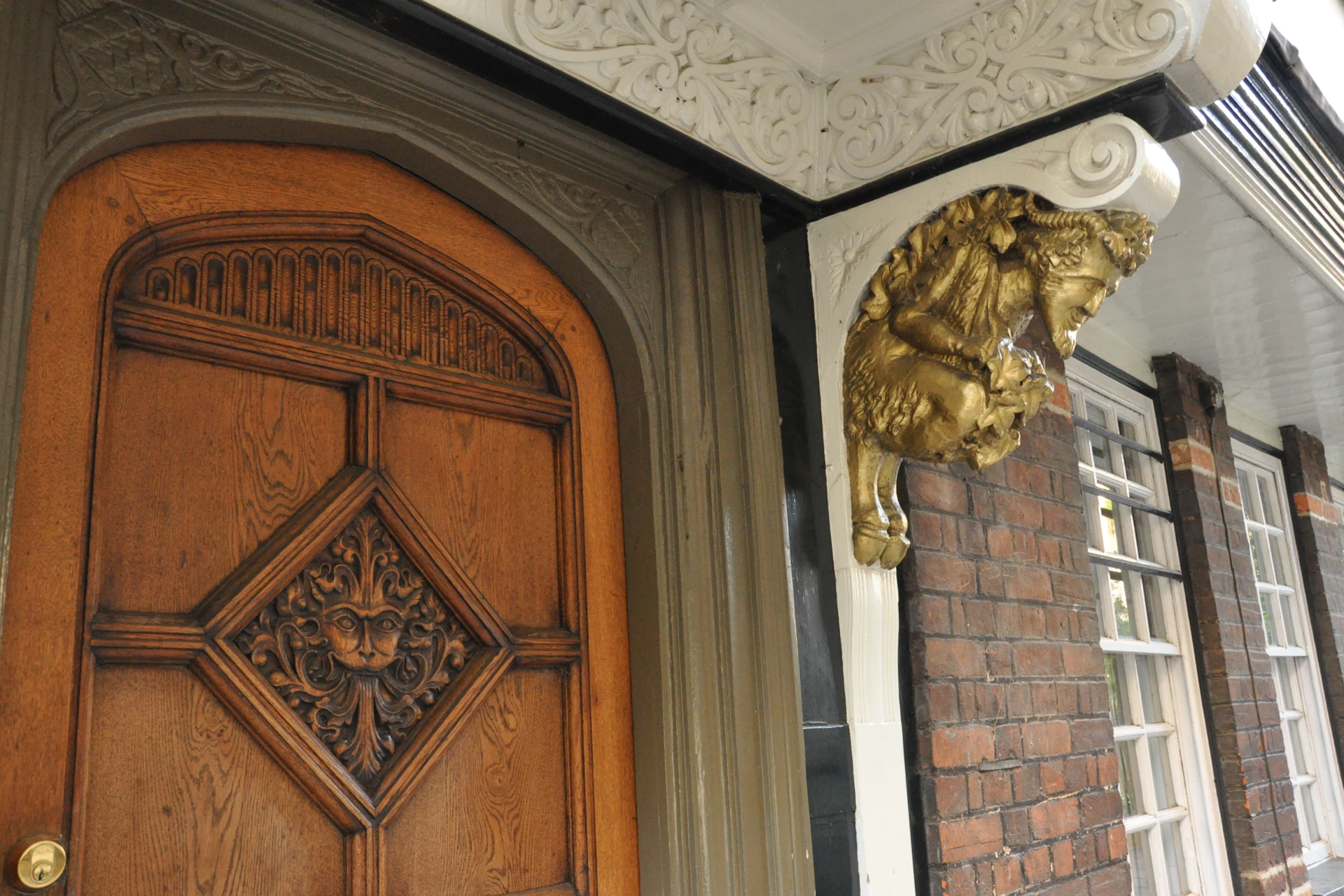 A wooden door with intricate carvings next to a decorative corner featuring a gold goat sculpture and detailed white molding.