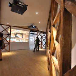 Människor i en museumskorridor med trägitterväggar, som observerar illustrerade displayer och projicerade bilder.