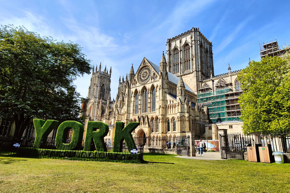 A large Gothic cathedral with intricate architecture is behind a grassy area with a green bush sculpture spelling "YORK."