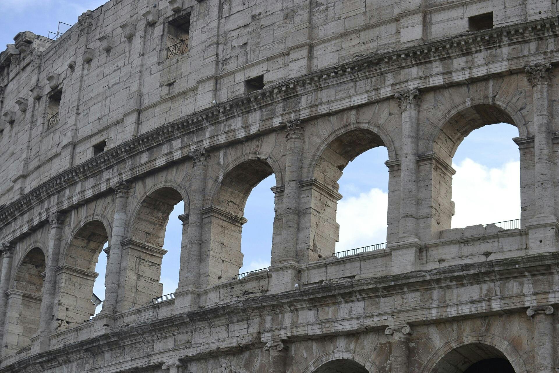 Руины древнеримских сооружений с колоннами и арками, с куполообразной церковью на заднем плане под ярким голубым небом.