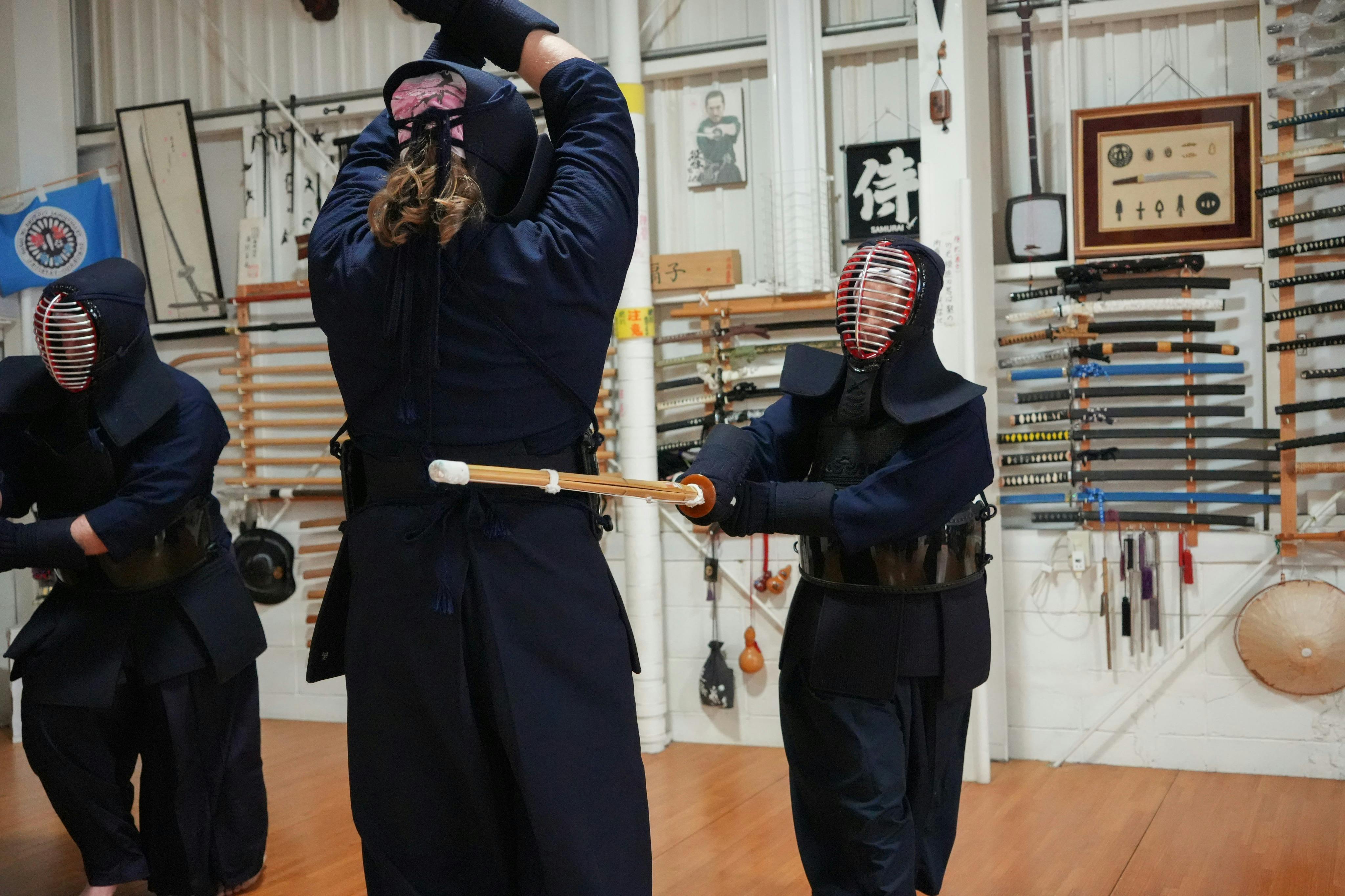 壁に様々な武道の武器が飾られた部屋で練習している剣道道具を着た2人。
