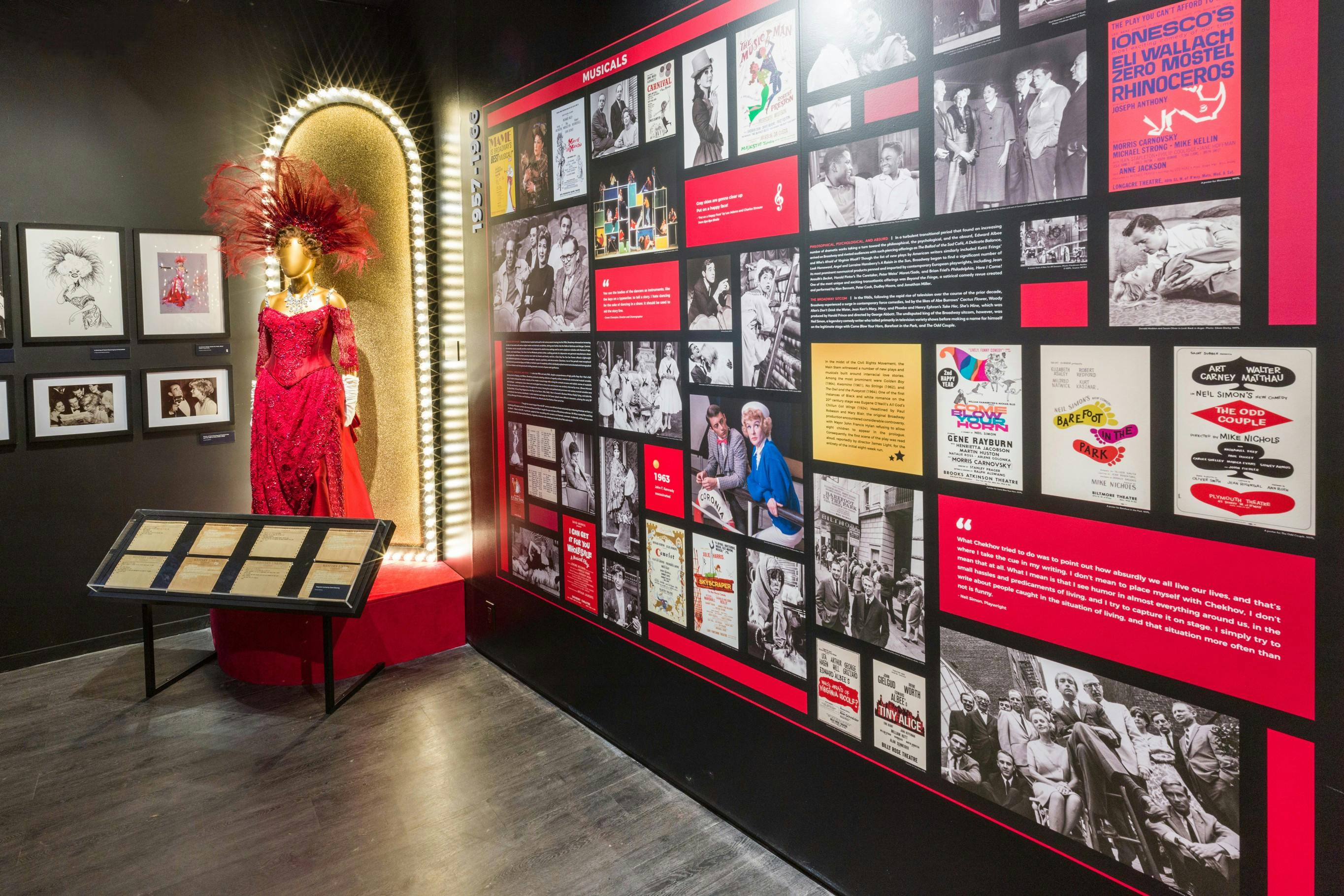 Expozice muzea s červenými flitrovanými šaty s peřím na figuríně a stěnou historických fotografií a textových displejů.