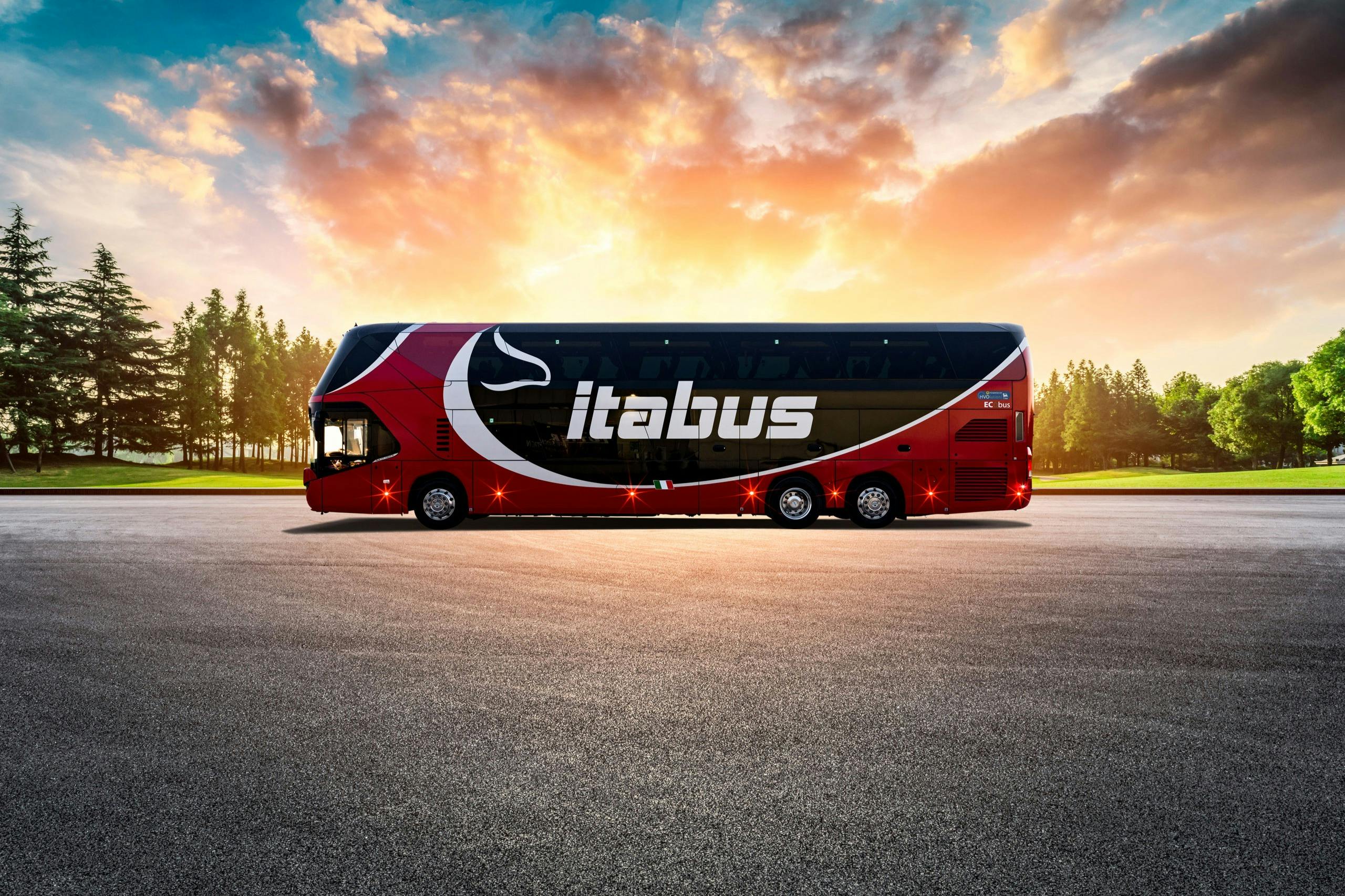 一辆标有“Itabus”的红色双层巴士停在铺面区域，背景是日落天空和树木。