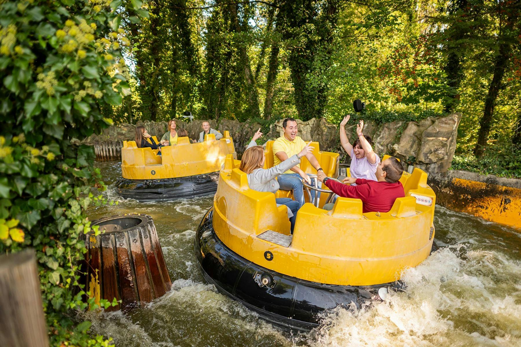People enjoying a river rapids ride in yellow circular boats surrounded by greenery and water.