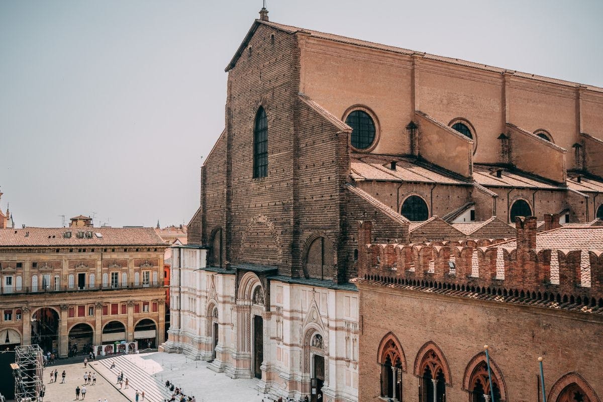 A large, historic brick church with a white and brown facade, located in a city square with people walking around.