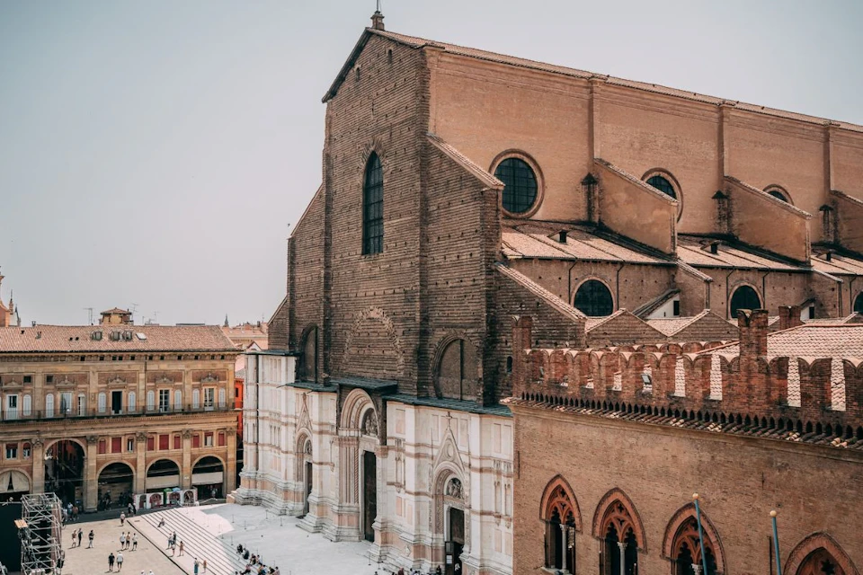 A large, historic brick church with a white and brown facade, located in a city square with people walking around.