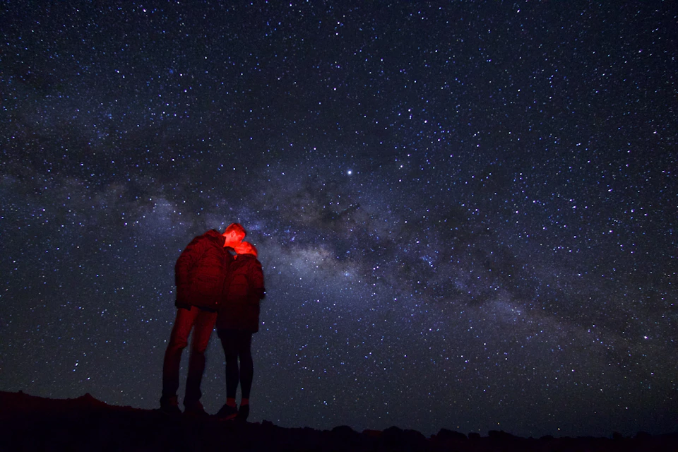 Two people stand closely together under a star-filled night sky with the Milky Way galaxy visible.