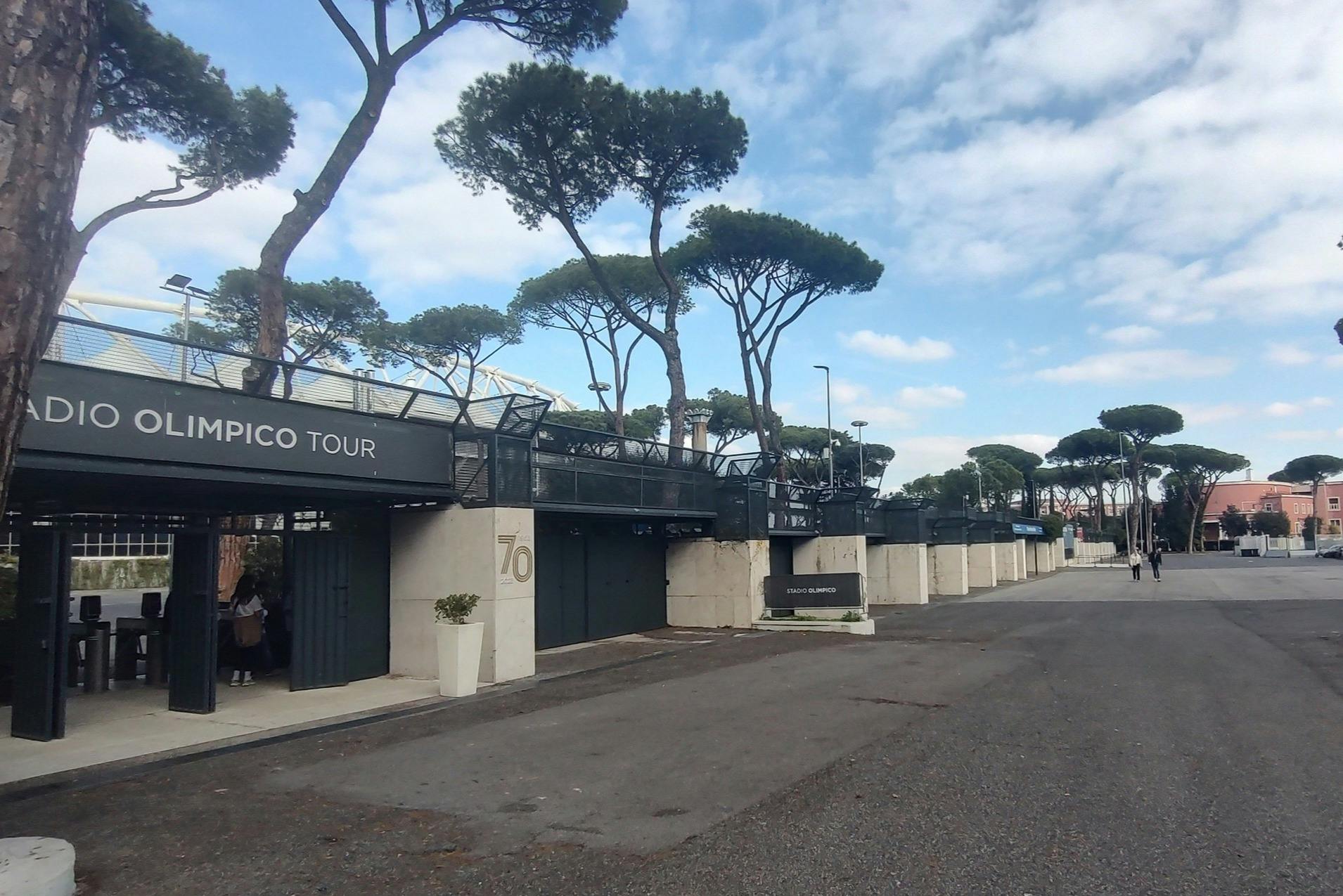Toegangsgebied tot een tourlocatie met moderne architectuur, dennenbomen en een heldere hemel.