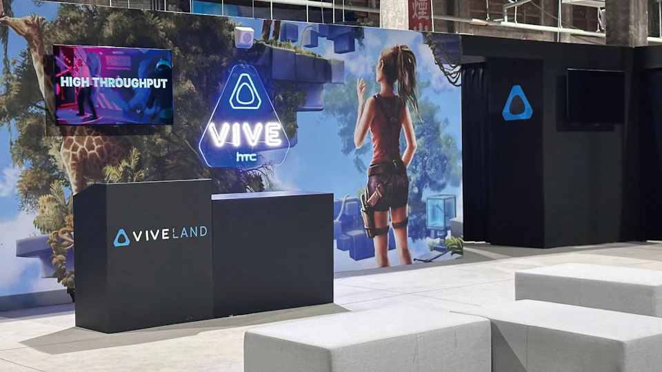 A promotional booth displaying HTC Vive branding with a large mural of a game character in a jungle setting.
