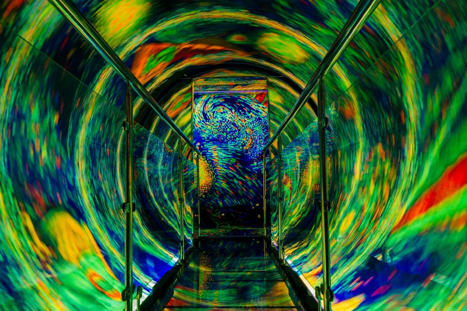 A walkway with metal railings surrounded by swirling, colorful lights resembling a vortex or tunnel effect.