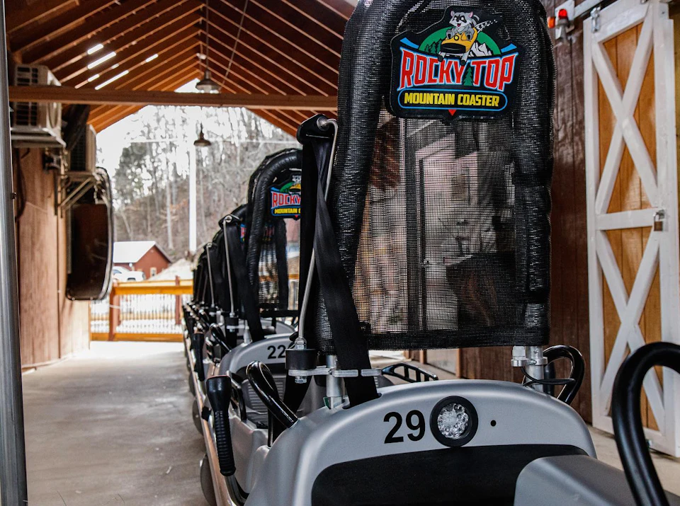 Seatbacks of rollercoaster cars under a wooden canopy labeled "Rocky Top Mountain Coaster," with car numbers visible.