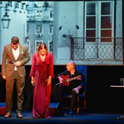 Två artister bugar på scenen med en svartvit stadsbild som bakgrund. Två musiker sitter och spelar gitarr bakom dem.