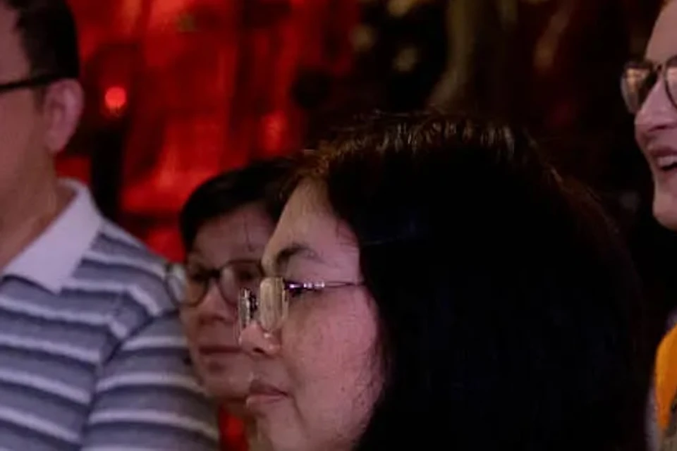 A group of people observing something off-screen in a dimly lit environment, with a backdrop featuring warm lighting and decor.