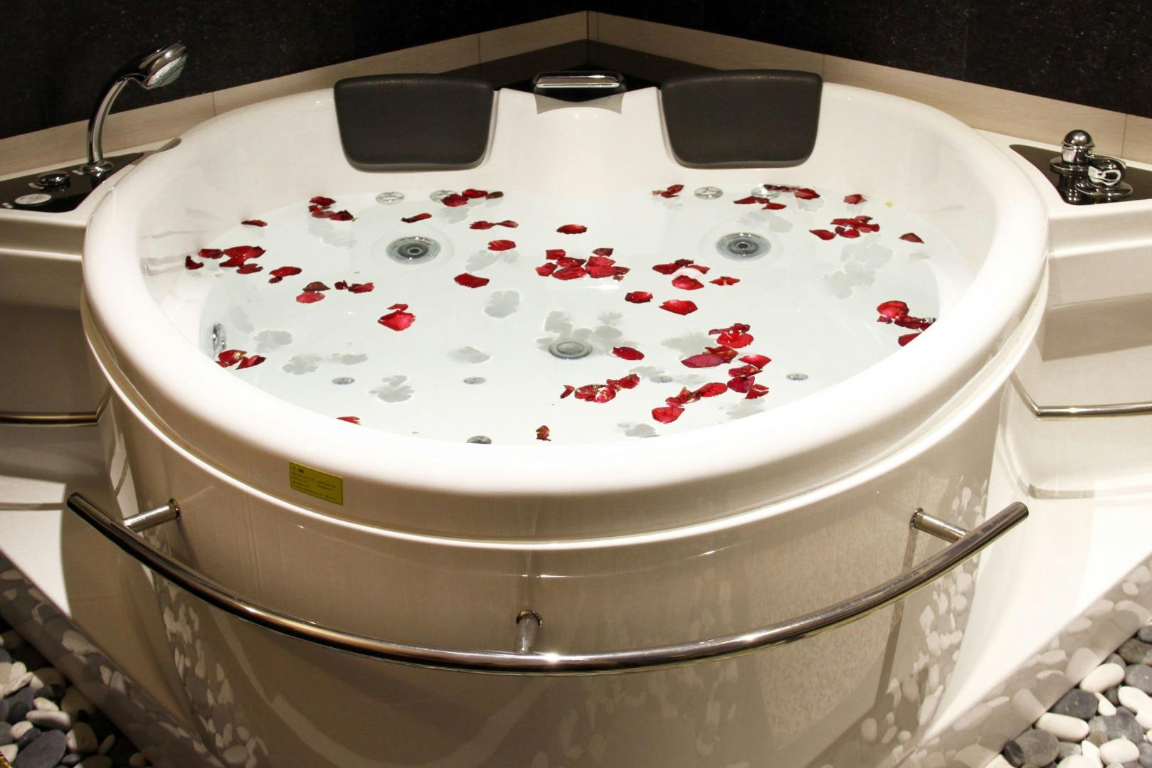 Okrągła wanna jacuzzi wypełniona wodą, płatki róży unoszące się na powierzchni i zagłówki na krawędzi.