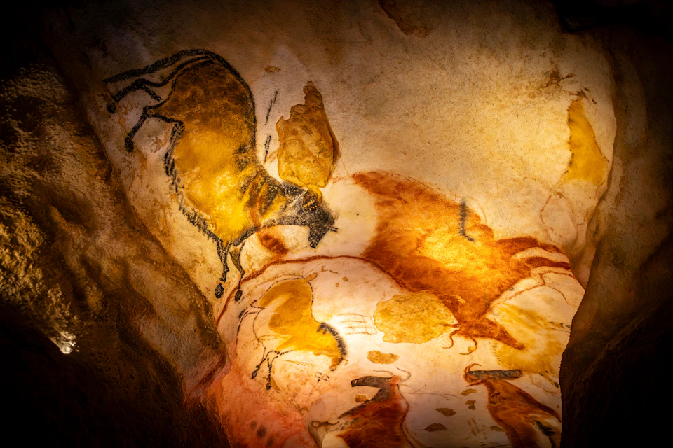 Cave painting depicting animals, featuring yellow and orange hues with black outlines, on a textured rock surface.