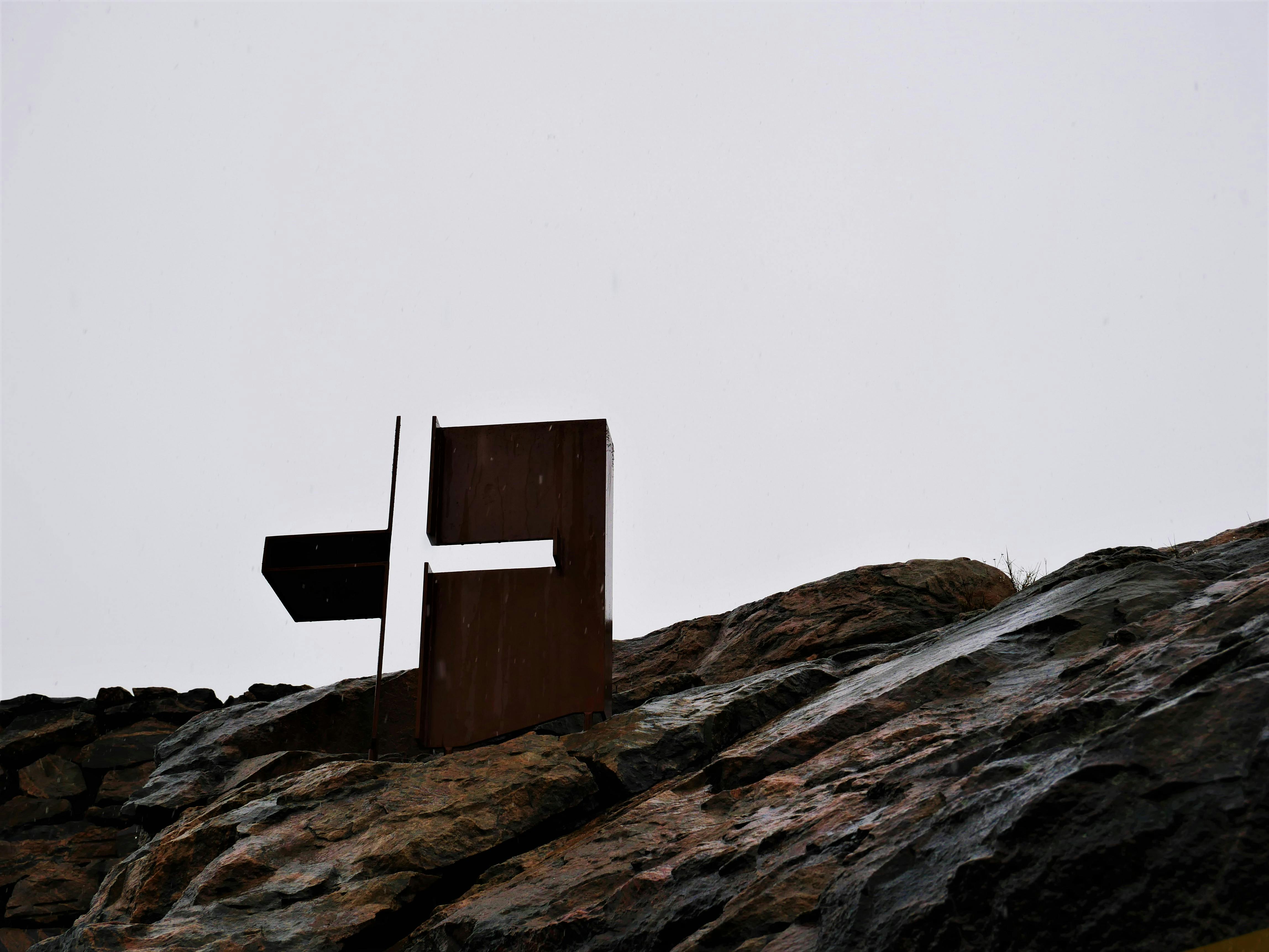 Metallische abstrakte Skulptur auf einem felsigen Hügel unter einem bewölkten Himmel.