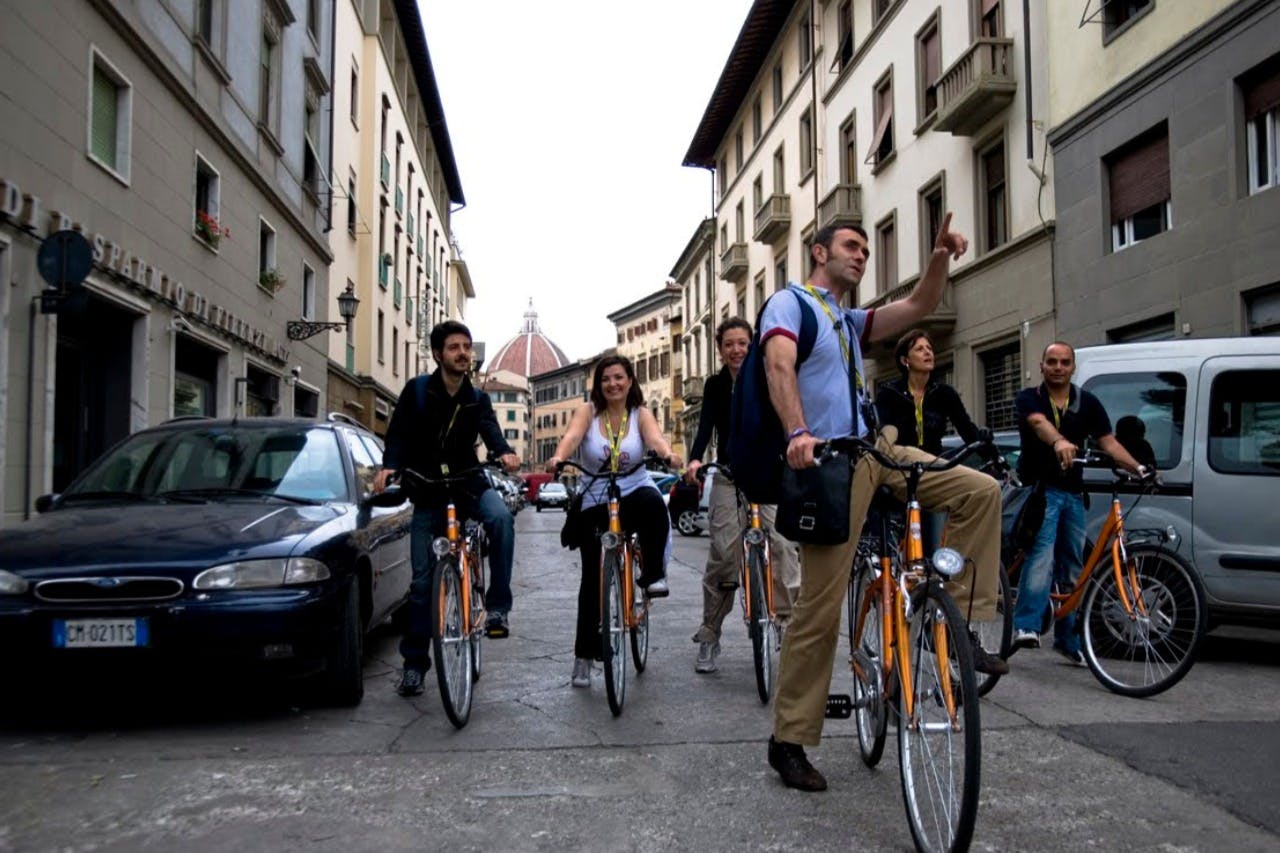 Group of people riding bicycles down a street between buildings, with a dome building visible in the background.