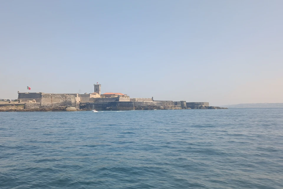 A stone fortress with a tower on a coastline seen from the sea under a clear blue sky.